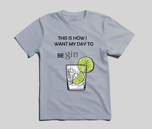 A light blue crewneck t-shirt with a graphic print that reads 'THIS IS HOW I WANT MY DAY TO BE gin' above an illustration of a highball glass with ice, a lime slice, and a lime wheel garnish, shown on a neutral gray background.