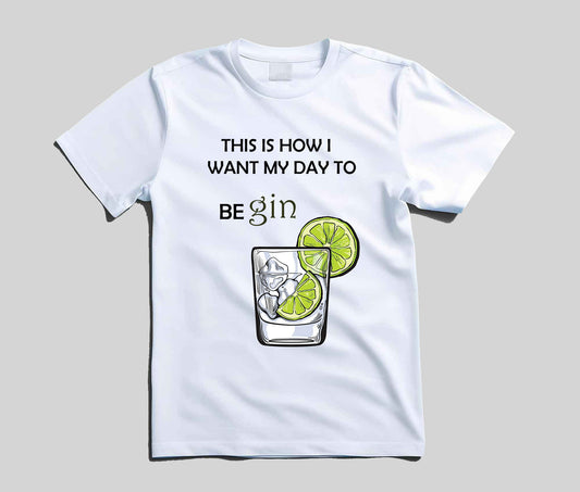 A white short-sleeve t-shirt with a graphic print that reads 'THIS IS HOW I WANT MY DAY TO BE gin' above an illustration of a gin glass with lime slices, shown on a neutral gray background.